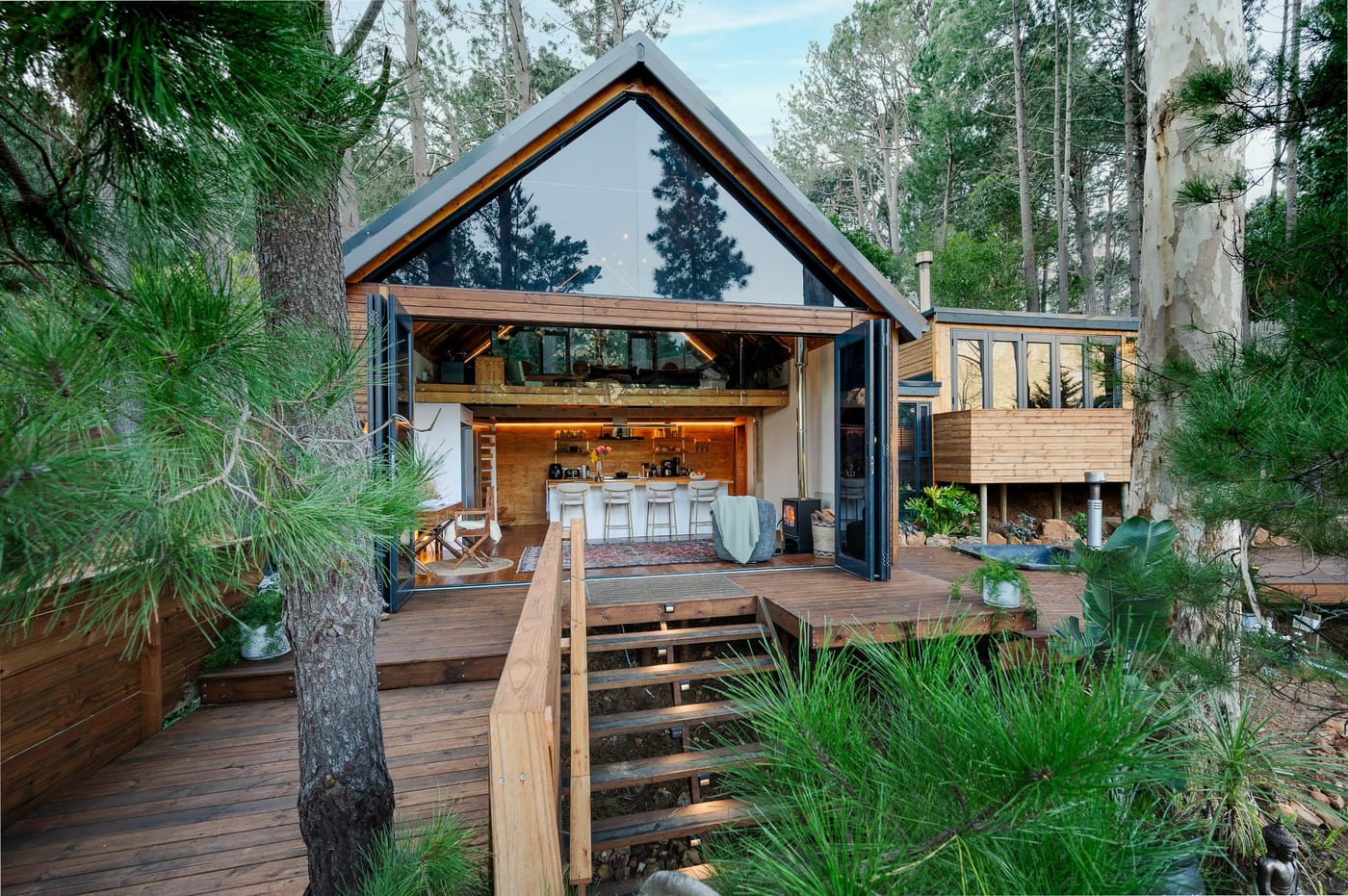 The A-frame thrown open at dusk, the kitchen glowing beneath the glazed gable