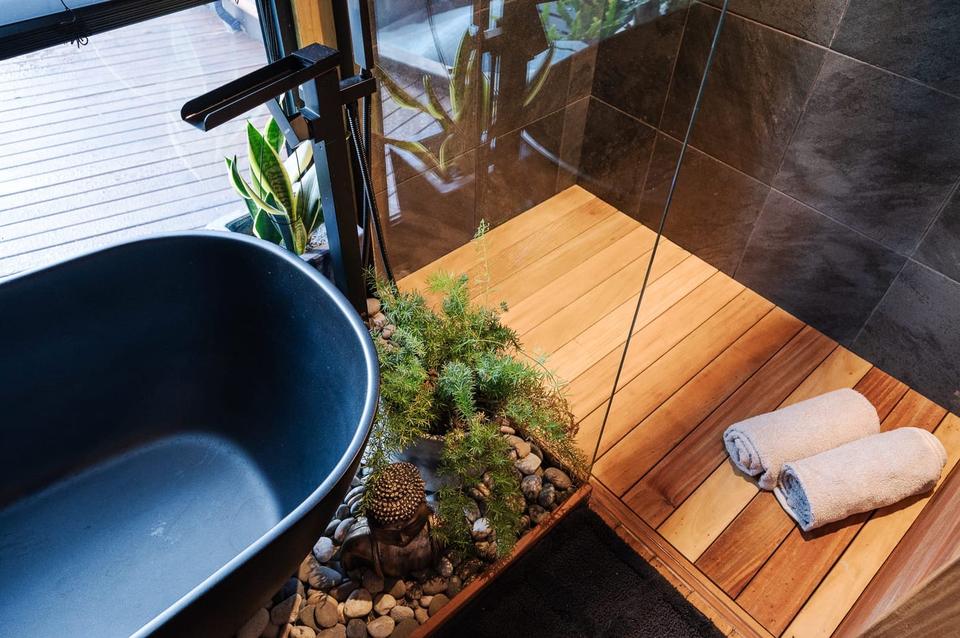 The bath from above, a fern and pebble planter alongside and towels rolled on timber