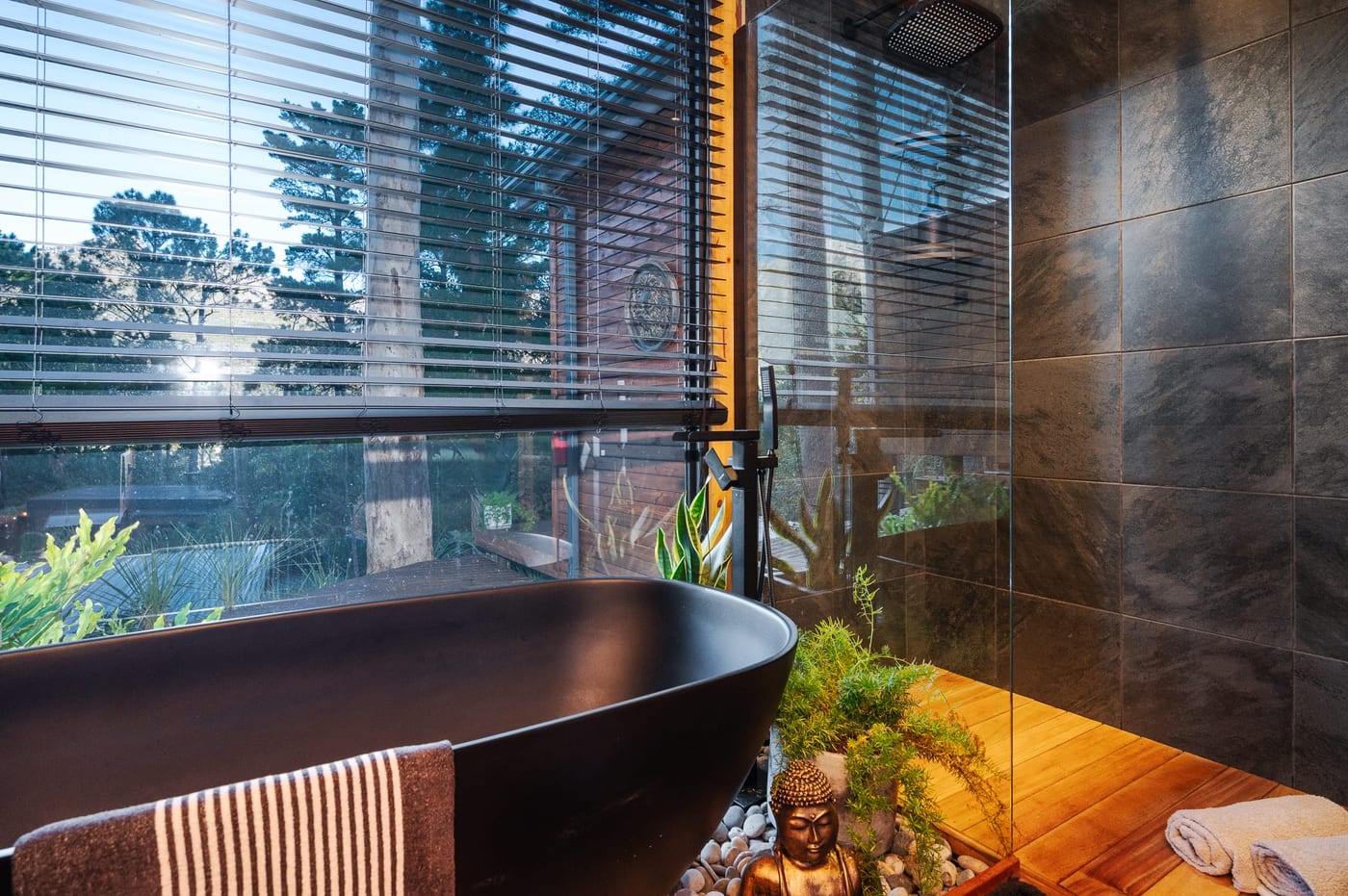 The black bath beside the rain shower, blinds open to the pines