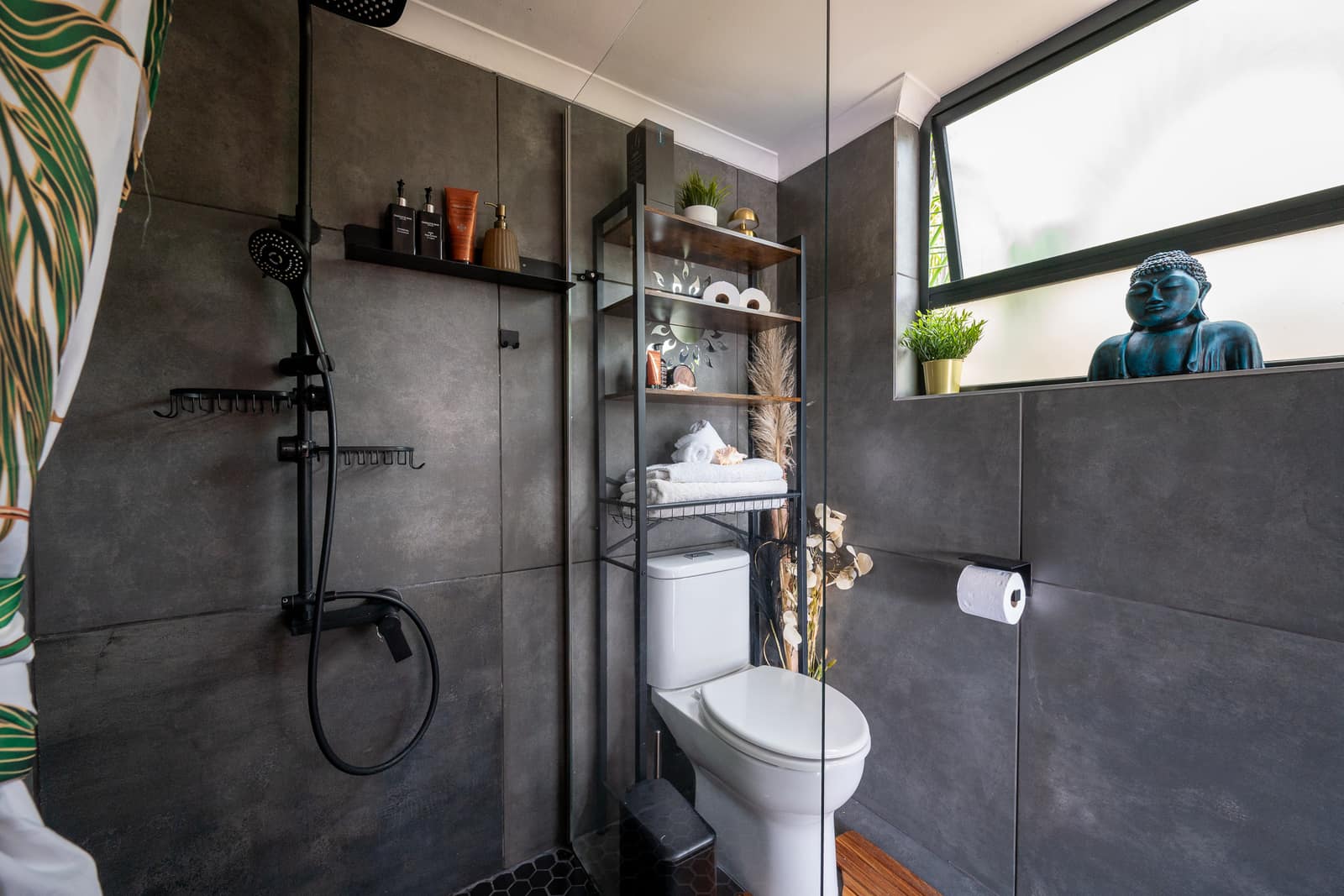 The walk-in rain shower on black hex tile, a turquoise Buddha on the window ledge beyond