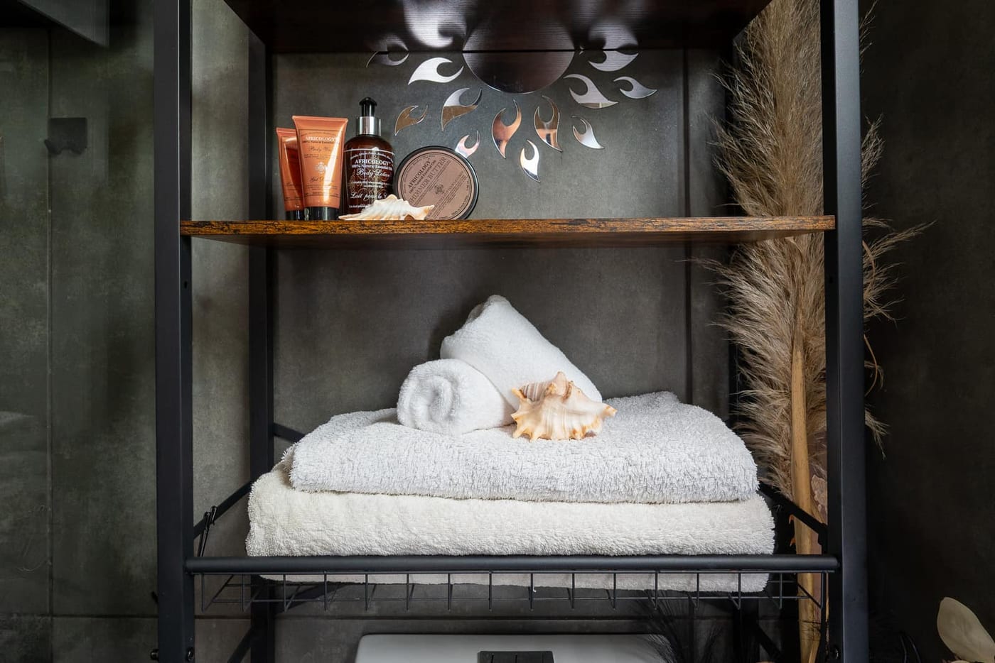Africology amenities and a conch shell on the timber shelf, towels folded below