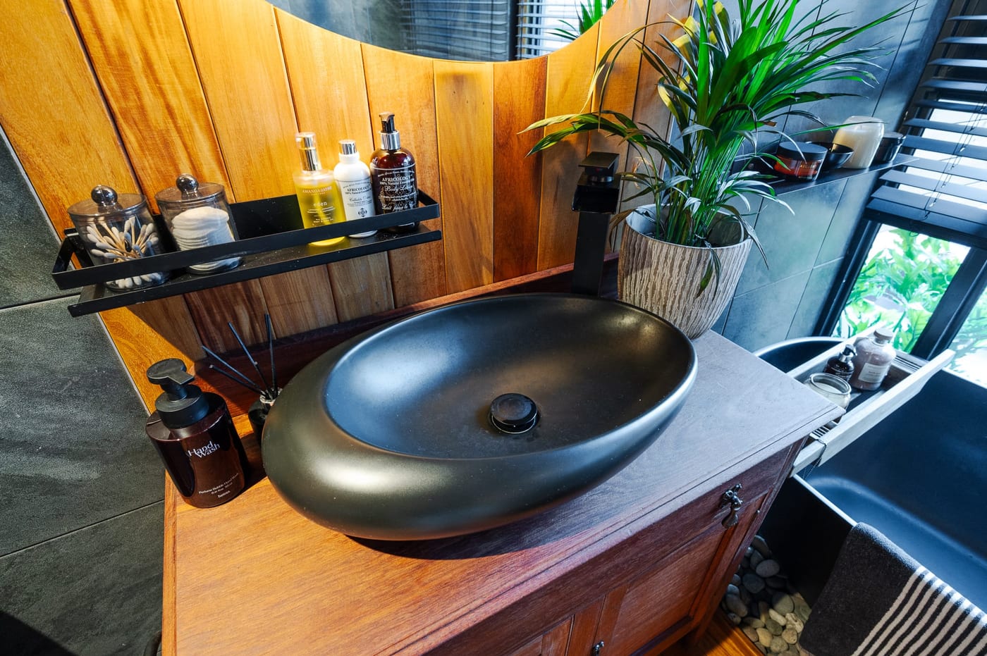 The black stone basin on its timber washstand, amenities on a slim black shelf
