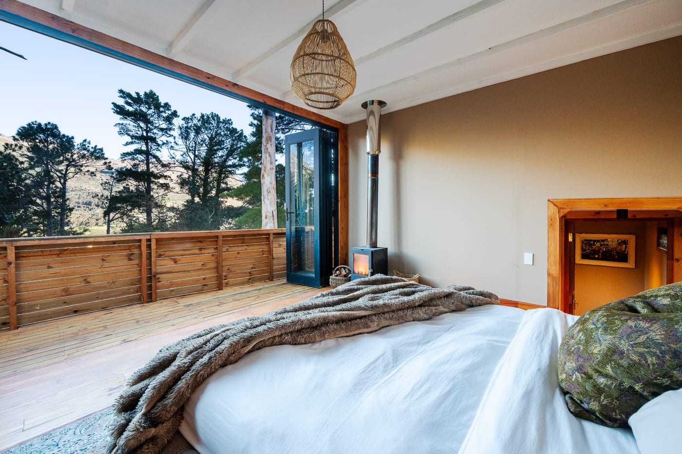 The bedroom with its glass wall slid fully open to the deck, stove lit and mountains beyond