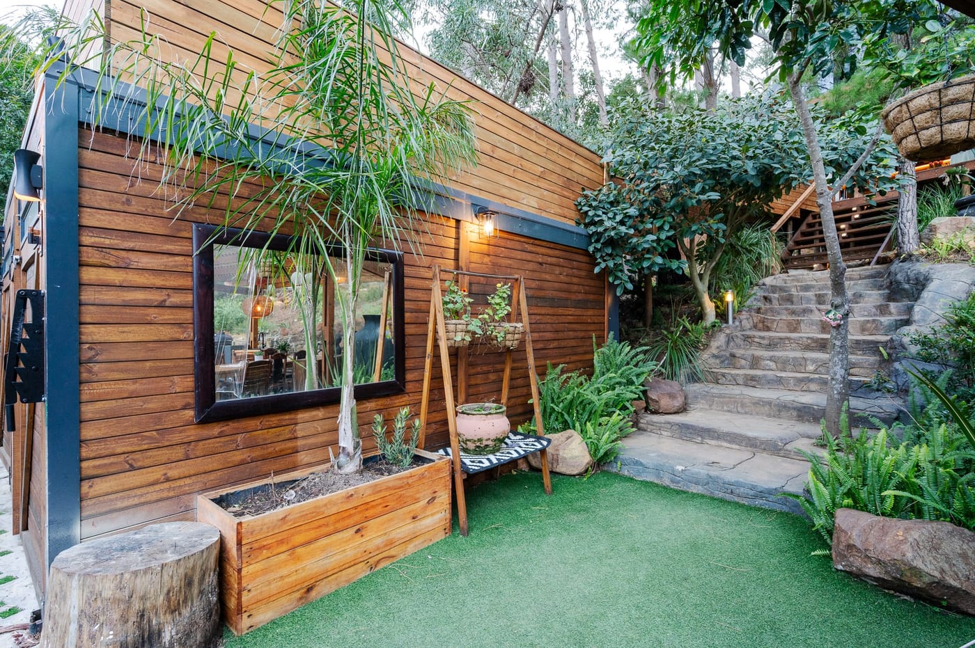 A framed mirror on the timber cladding, stone steps rising through ferns alongside