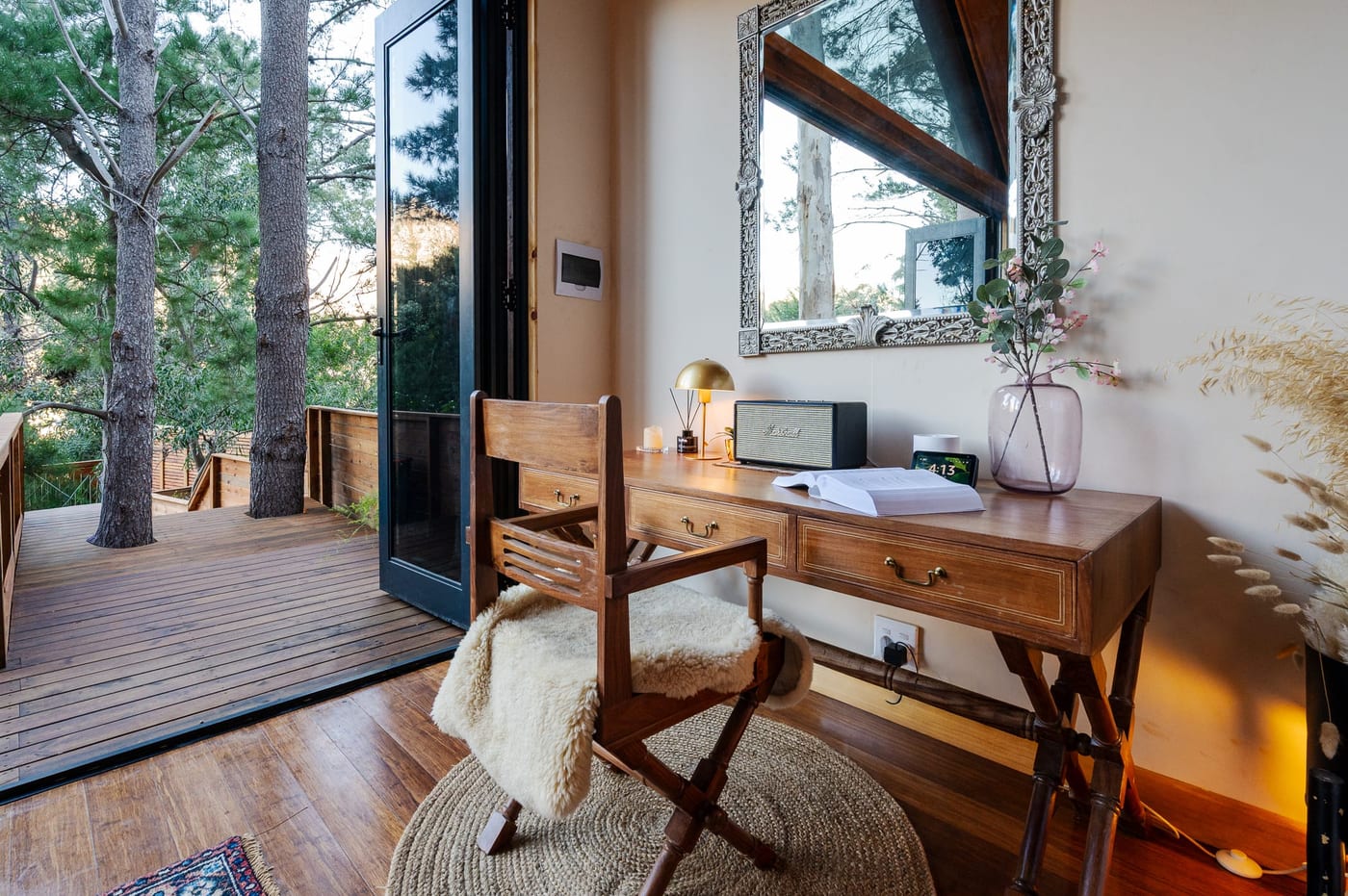 A writing desk beside glass doors opening onto the deck and trees