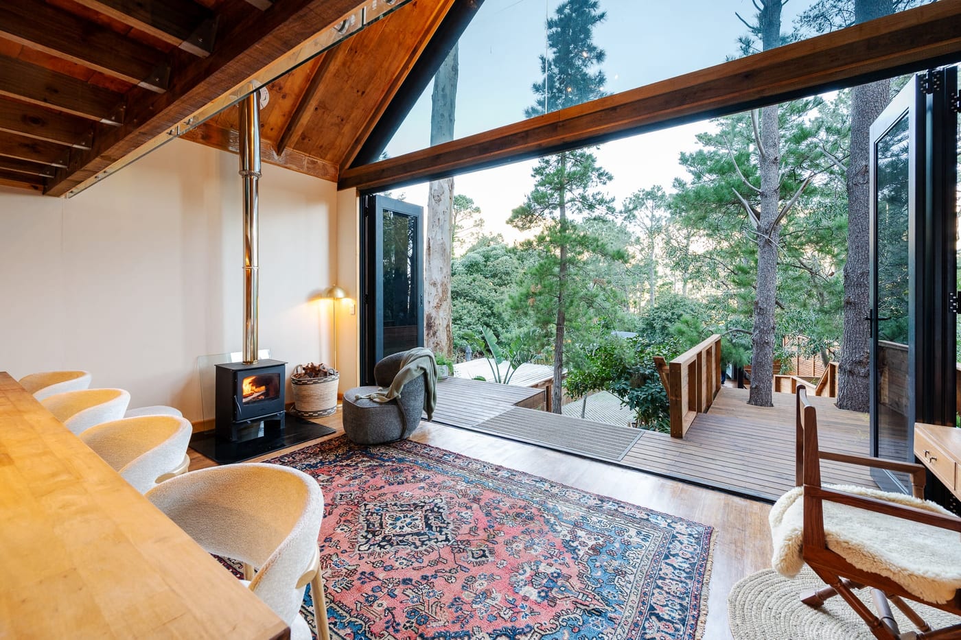 Dining chairs along the counter, the stove lit and the deck open to the pines
