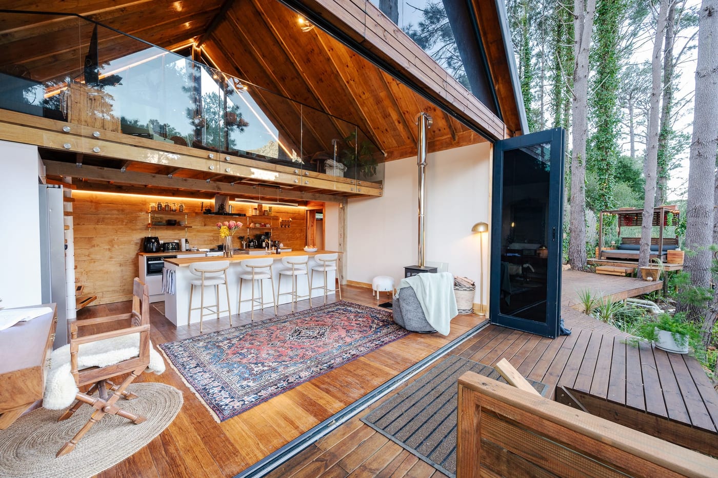 The bifolds folded right back at dusk, kitchen and fire glowing, pergola lounge beyond