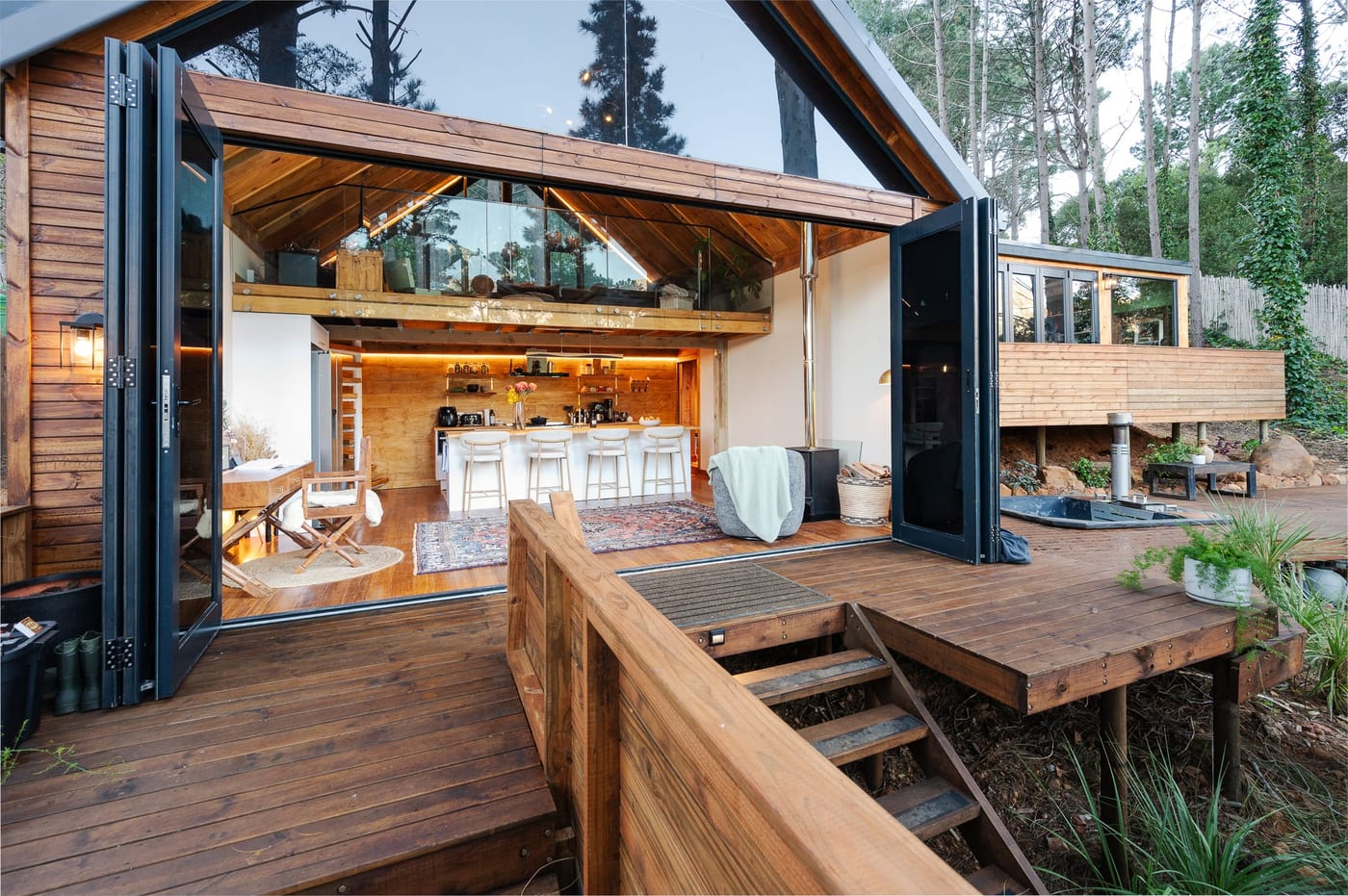Bifold doors folded fully open onto the deck, the kitchen and fire glowing inside