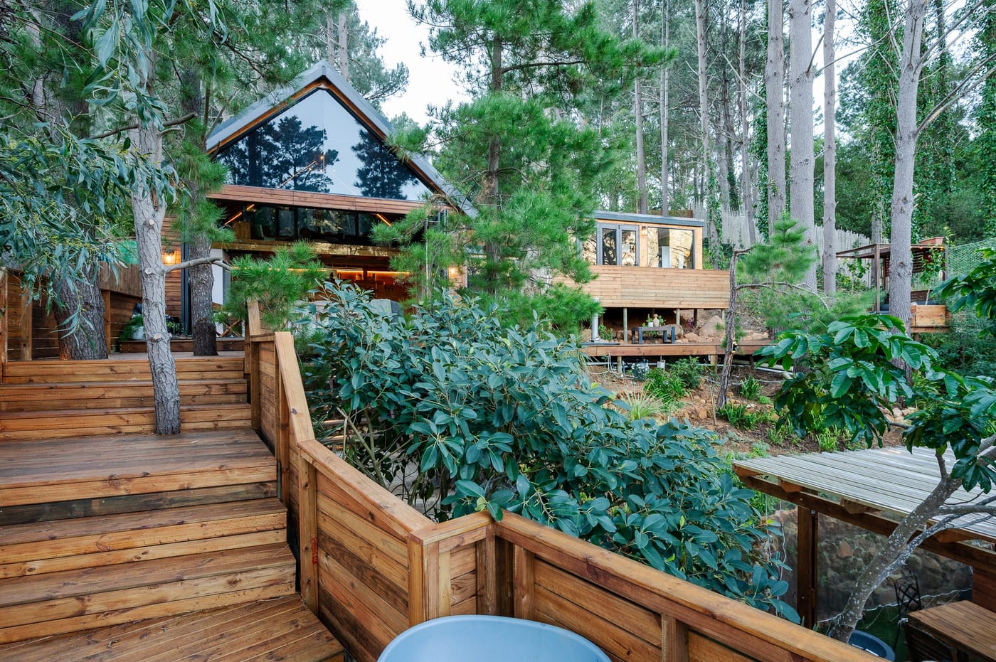 The A-frame studio lit from within at dusk, seen across the timber decks