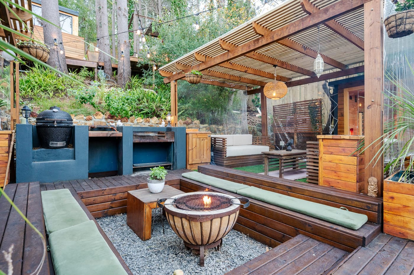 The sunken fire pit lit between cushioned benches, braai and kamado alongside