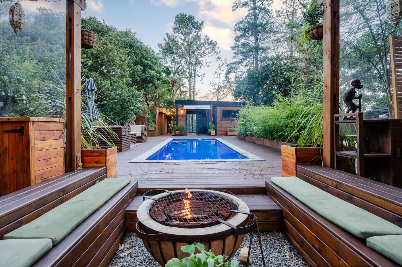 Looking straight down the pool between the pergola posts, the fire pit lit in front