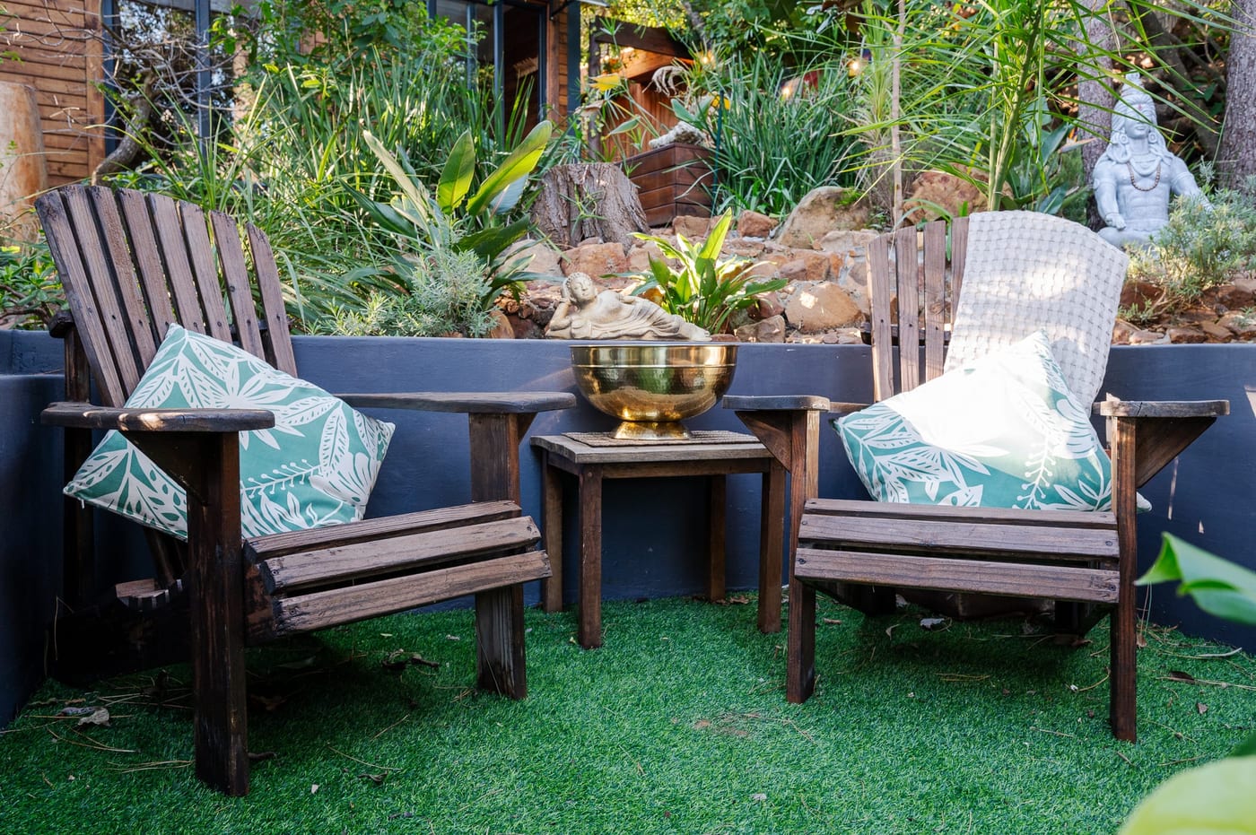 Two weathered chairs beside a brass bowl and a reclining Buddha