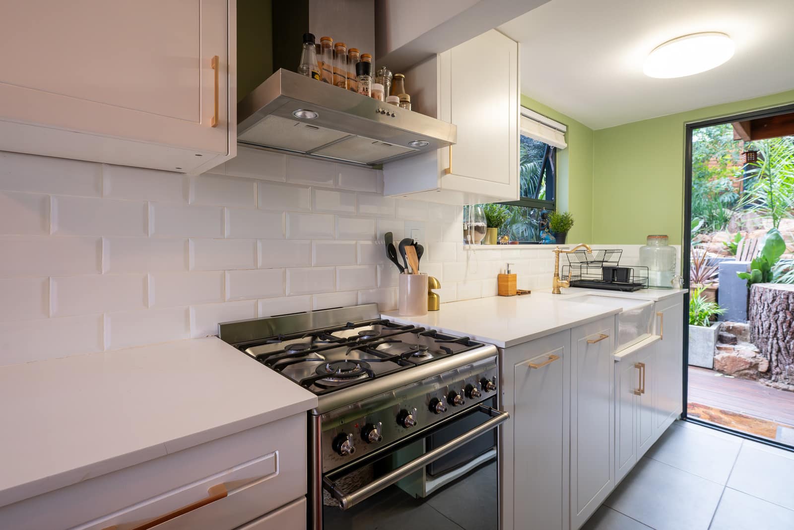 The white shaker kitchen with its gas range and bevelled tile, the door open to the garden