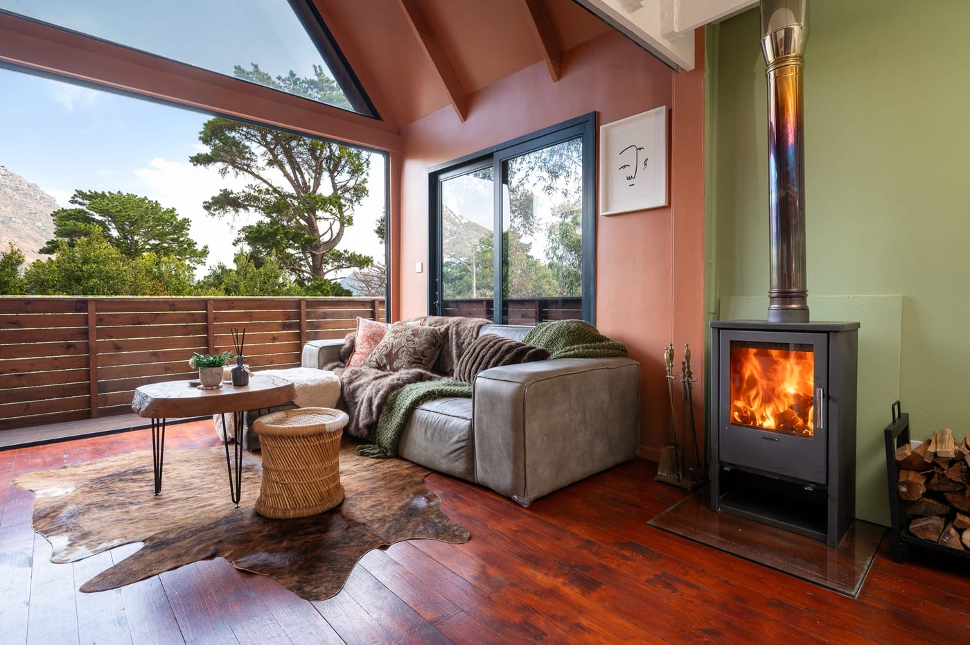 The wood stove lit beside the leather sofa, glass framing the mountains
