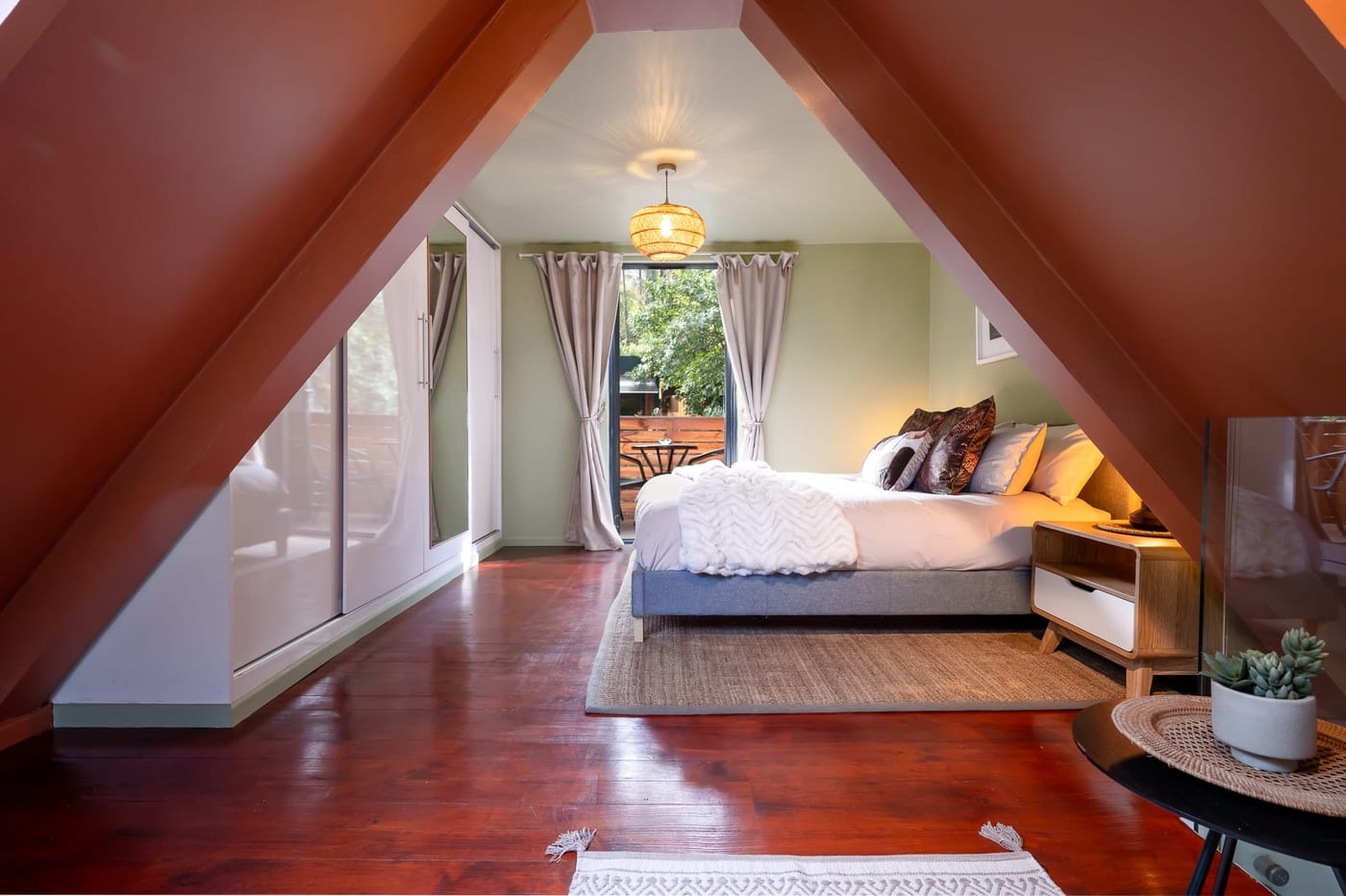 The loft bedroom down its length, terracotta A-frame beams over the bed and balcony door