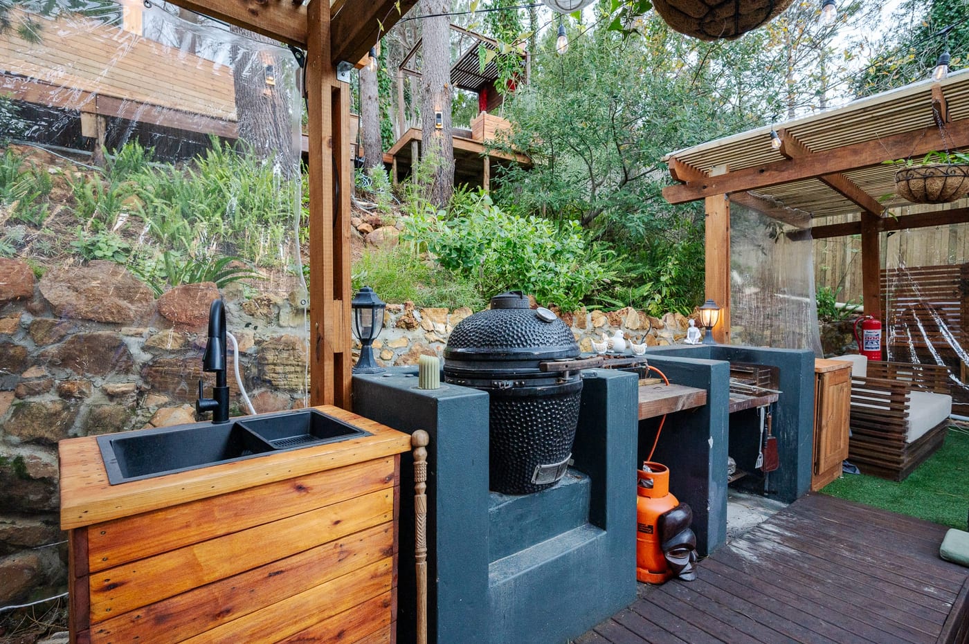 The outdoor kitchen — timber sink unit, kamado grill and braai under the pergola