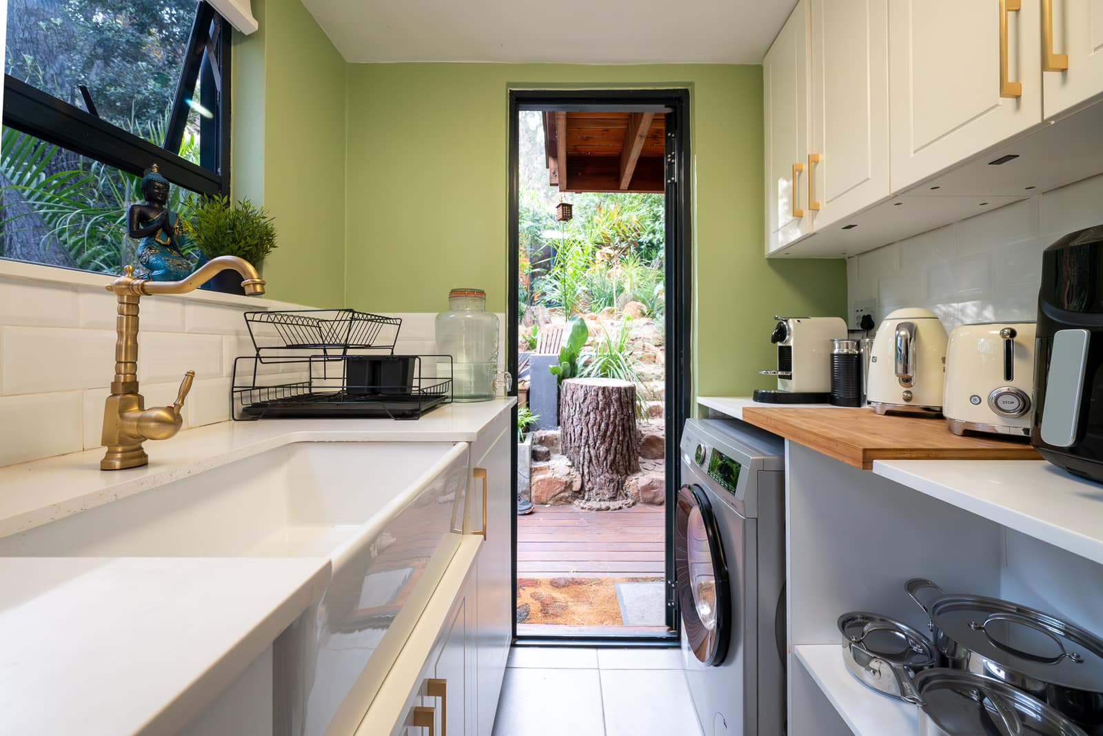 The scullery — brass tap over a farmhouse sink, laundry alongside and the door open to the deck