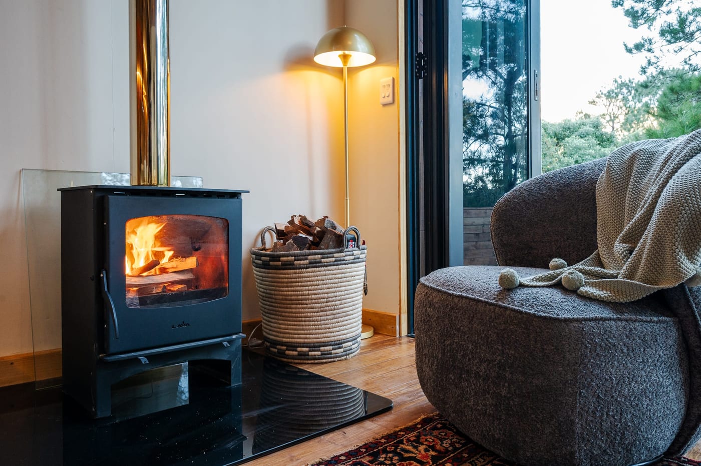 The wood-burning stove lit beside an armchair and a basket of firewood